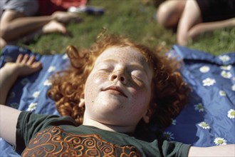 Child, boy, fair-skinned, with red hair and freckles sleeps in a meadow unprotected in the first