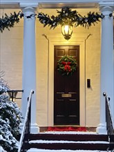 Festive front porch with holiday garlands wrapped around the columns, a wreath hanging on the door,