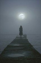 Silhouette of a lonely, sad woman on a concrete footbridge on a foggy full moon night, symbolic