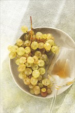 A branch of white grapes, on a gray plate, with a glass of white wine, top view, natural light,