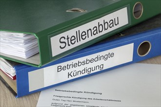 Cancellation in front of folders labelled STELLENABBAU and BETRIEBSBEDING KÜNDIGUNG (symbolic