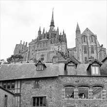 A black and white photo of a Gothic church with stone houses in the foreground, Le