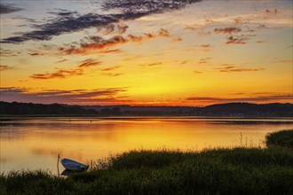 Calm sunset over a lake with a boat in the middle of high meadows, Rügen