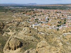 Expansive view of a village surrounded by hilly, rocky landscapes under a clear sky, aerial view,