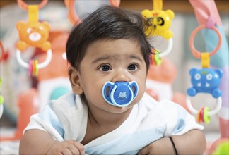 Baby boy playing lying on bed with pacifier on mouth