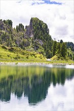 A clear mountain lake reflects the surrounding trees and mountains under a cloudy sky, Penken,