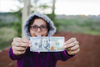 Amazed woman showing 100 dollar bill outdoors