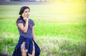 Beautiful young woman calling by cell phone on the grass outdoor. Young girl calling phone on the