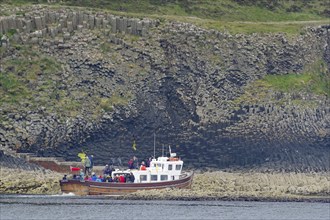 A boat loaded with people approaches the rocky coast, tourist boat, Hebrides Overture, Staffa