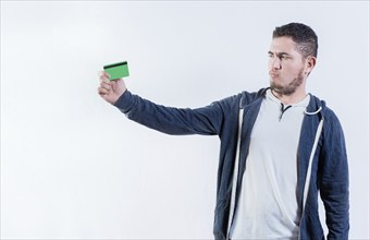 Unsure person holding a credit card isolated. Confused man holding and looking at credit card