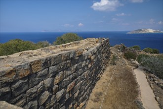 Ruin wall in an arid landscape with a view of the sea and a coastline in the background,