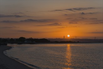 Peaceful coastal scene at sunset, the light reflects in the calm water while the sky glows in warm