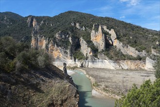 A river flows through a rocky landscape surrounded by high, steep cliffs and wooded mountains under