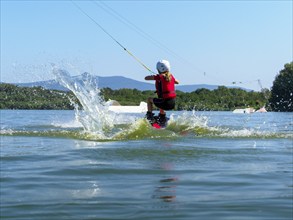 Boy or girl, jump over jump with wakeboard, red life jacket and water sports, water skiing in