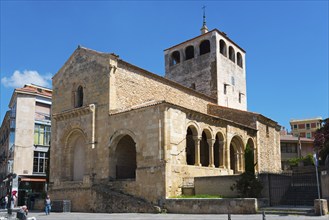 Romanesque church with high tower and arches, built of stone, under a blue sky in sunny weather,