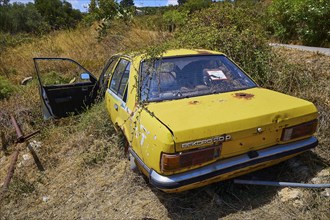 Yellow, old car left behind, overgrown with weeds in summer weather, wrecked vehicle, Crete, Greek