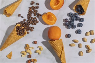 Ice cream cones with coffee beans, apricots, blueberries, pistachios and nuts on a marble