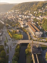 Aerial view of a town with a river and bridges, surrounded by green hills at sunset, with typical