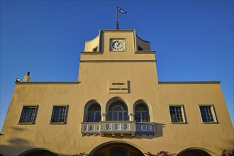 Historic building with clock tower and Greek flag in warm evening light, town hall, Dimarchio,