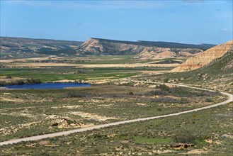 Landscape with fields, hills and a lake under a clear blue sky, Bardenas Reales Natural Park,