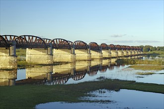 Long stone bridge with many arches crossing a calmly reflecting river, surrounded by nature,