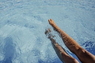 Legs dip into the blue water of a swimming pool, summer refreshment