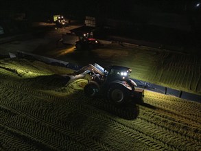 A tractor with front loader illuminates the night on a field while working, corn harvest, Dachtel,