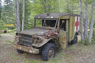 Rusty, old army ambulance, with Red Cross symbol between trees in the forest, former army camp,