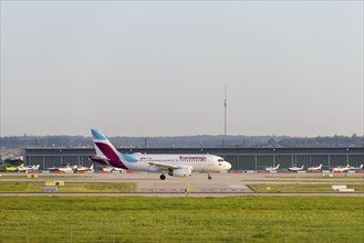 Eurowings aircraft landing on a runway in front of a hangar under a sunny sky, with the Stuttgart