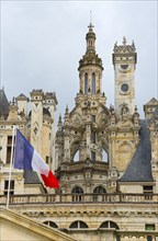 Detailed view of a historic castle with elaborate decorations and a French flag in the foreground,