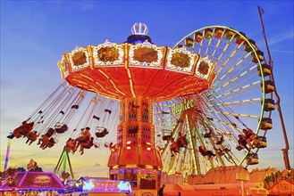 The colourfully illuminated Wellenflug chain carousel and the Ferris wheel in the evening, Cranger