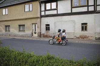 Symbolic photo on the subject of youth in the East. A boy and a girl ride a Simson moped past old