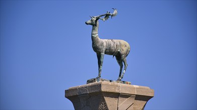 Bronze deer statue on a pedestal in front of a clear blue sky, Mandraki harbour, harbour area,