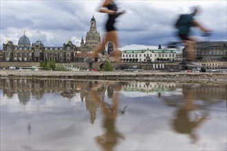 The silhouette of Dresden with a cyclist and a jogger and dark clouds behind the Church of Our Lady