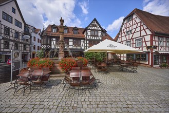 Market fountain with geraniums, half-timbered houses and outdoor areas of a restaurant with