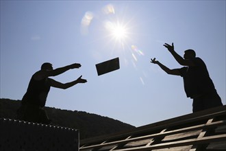 Silhouettes of two roofers throwing tiles at each other against the light