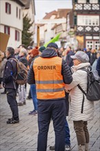 Two people talking at a demonstration, one in a police waistcoat, behind them a city street,