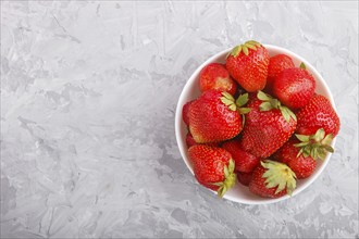 Fresh red strawberry in white bowl on gray concrete background. top view, flat lay, copy space