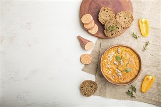 Sweet potato or batata cream soup with sesame seeds in a wooden bowl on a white wooden background