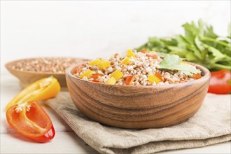 Buckwheat porridge with vegetables in wooden bowl on a white wooden background and linen textile.