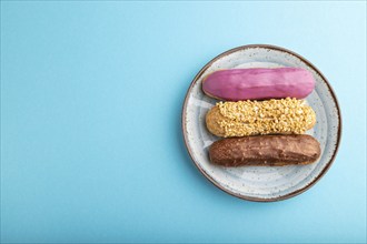 Set of eclair, traditional french dessert on ceramic plate on blue pastel background. top view,