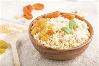 Bulgur porridge with dried apricots, raisins and cashew in wooden bowl on a white wooden background