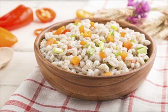 Pearl barley porridge with vegetables in wooden bowl on a white wooden background and linen textile