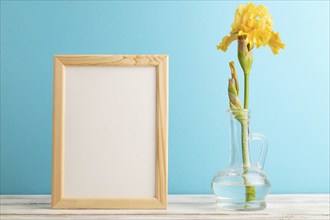 Wooden frame with yellow iris flower in glass on blue pastel background. side view, copy space,