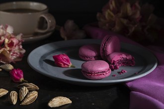 Purple macarons or macaroons cakes with cup of coffee on a black concrete background and pink