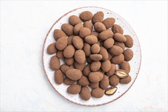 Almond in chocolate dragees on ceramic plate on white concrete background. Top view, close up, flat