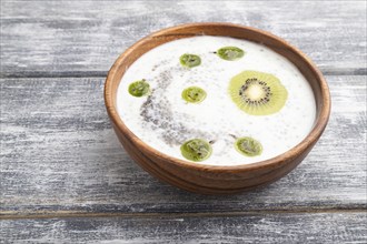 Yogurt with kiwi, gooseberry, chia and almonds in wooden bowl on gray wooden background. side view,