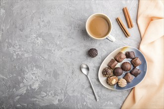 Different chocolate candies and a cup of coffee on a gray concrete background and orange textile.