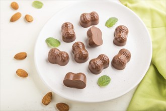 Chocolate candies with almonds on a white wooden background and green textile. side view, close up,