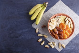 A plate with muesli, banana, dried apricots, dates, Brazil nuts on a black wooden background. top